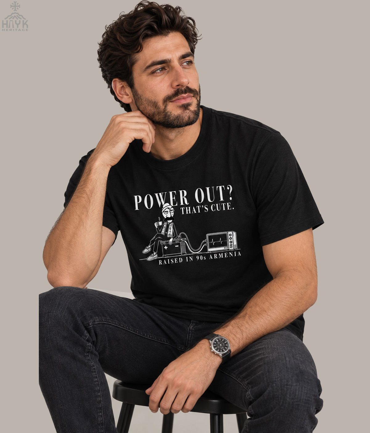Hayk Heritage "Norek Aram — Raised in the 90s" Armenian humor t-shirt: cartoon man sipping coffee on a car battery wired to an old TV, with "Power Out? That's Cute" and "Raised in 90s Armenia" text.